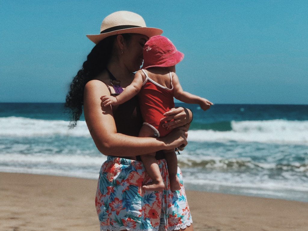 Une femme tenant son bébé sur ses bras à la plage.