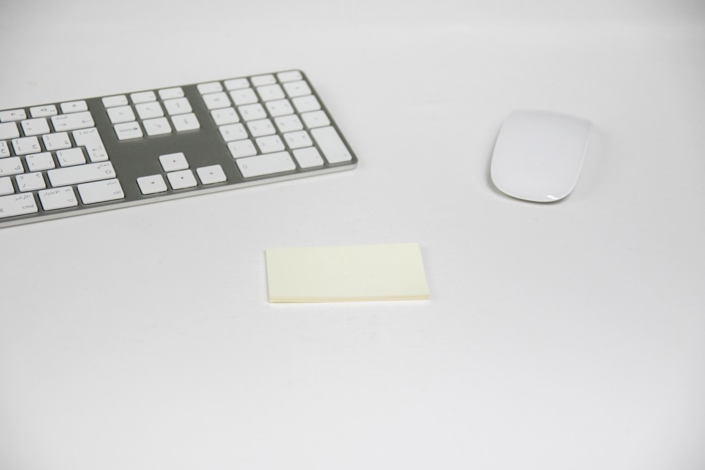 Un ratón y un teclado inalámbrico de ordenador junto a una lista de notas. Todo es de color blanco.