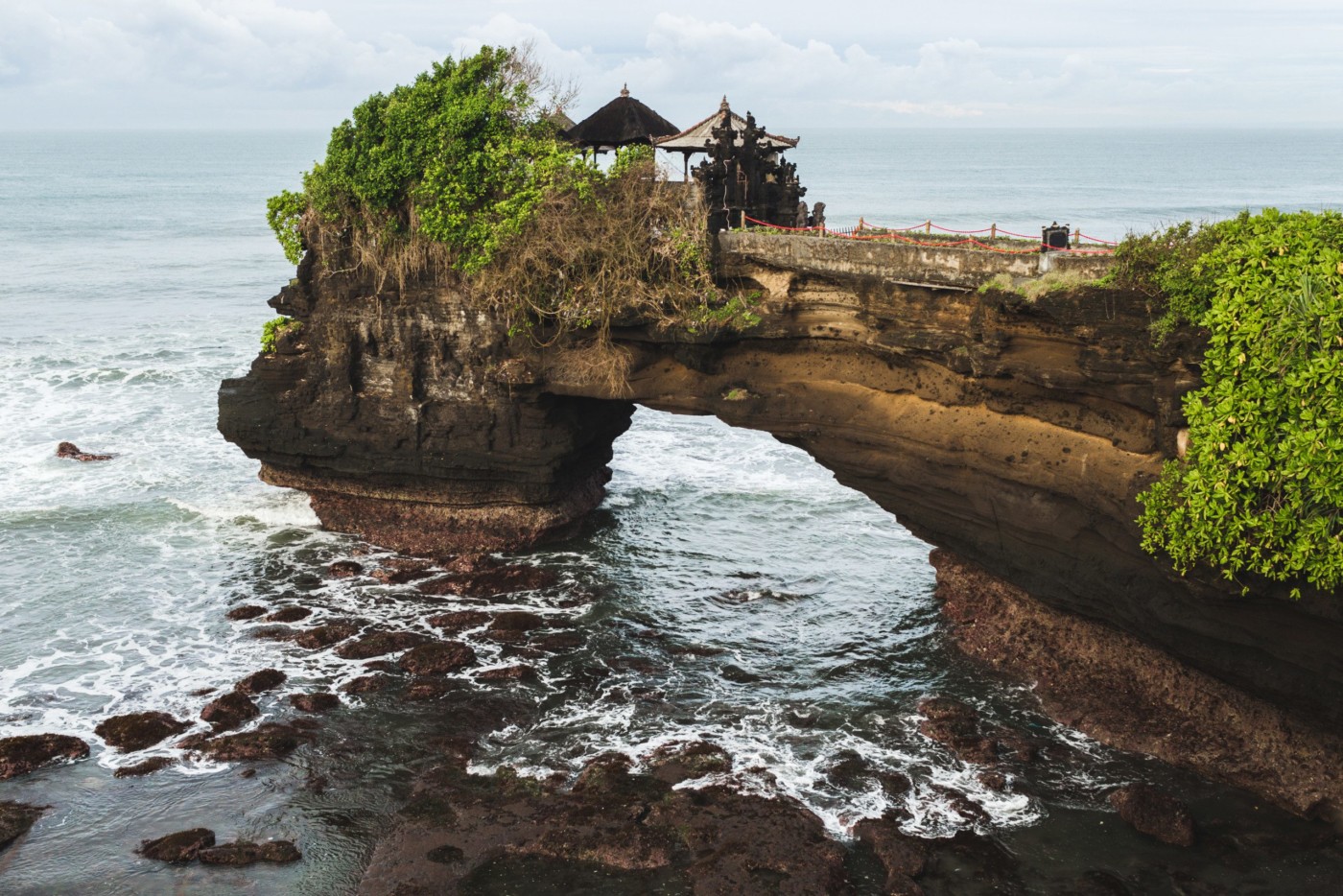 Sacred Balinese temple Tanah Lot. Pura Batu Bolong on the edge of a cliff at coastline with hole in the rock. Traditional style and architecture of Bali. Holy place for local indonesian people